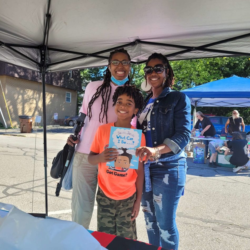 A child and two women smile with a book in hand